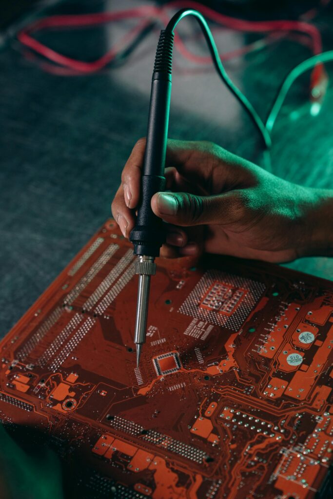 servıce Close-up of hand using soldering iron on motherboard, highlighting electronics repair work.